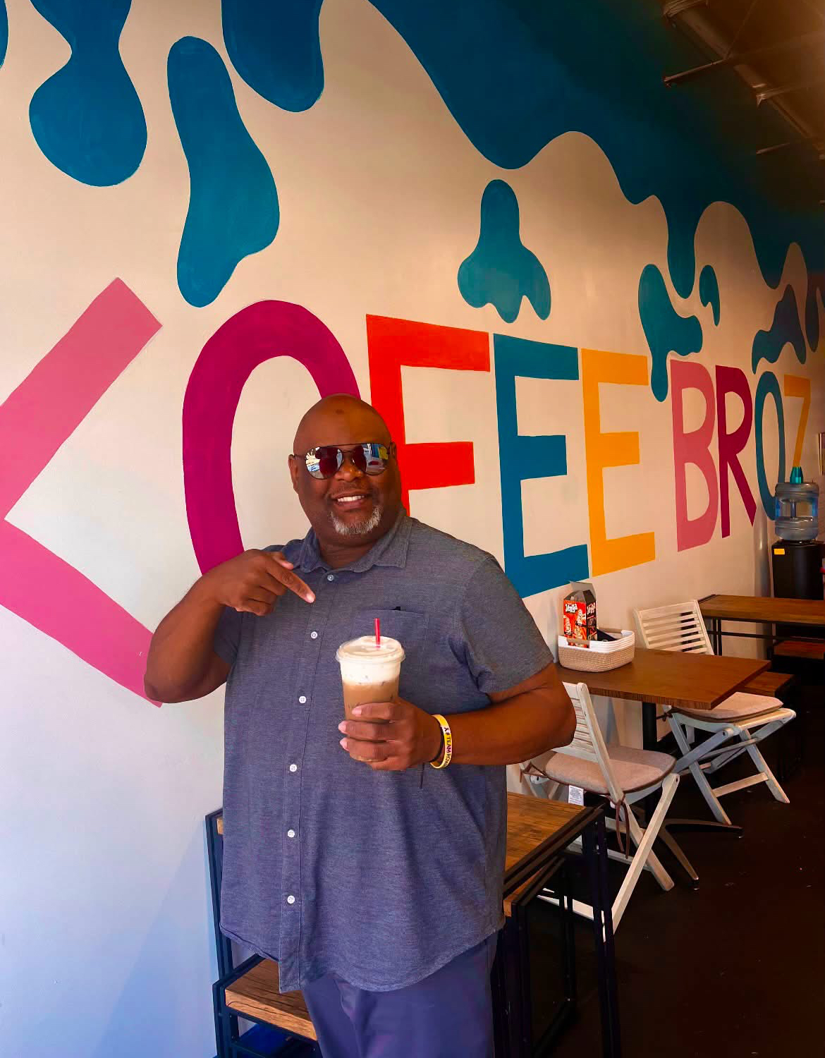 Customer holding an iced Kofee Broz drink in front of the mural
