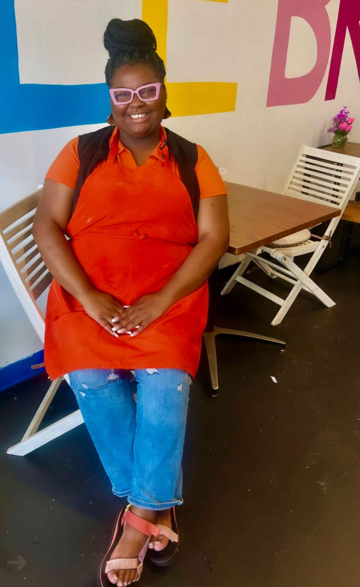 Team member in an orange apron smiling in front of the Kofee Broz mural