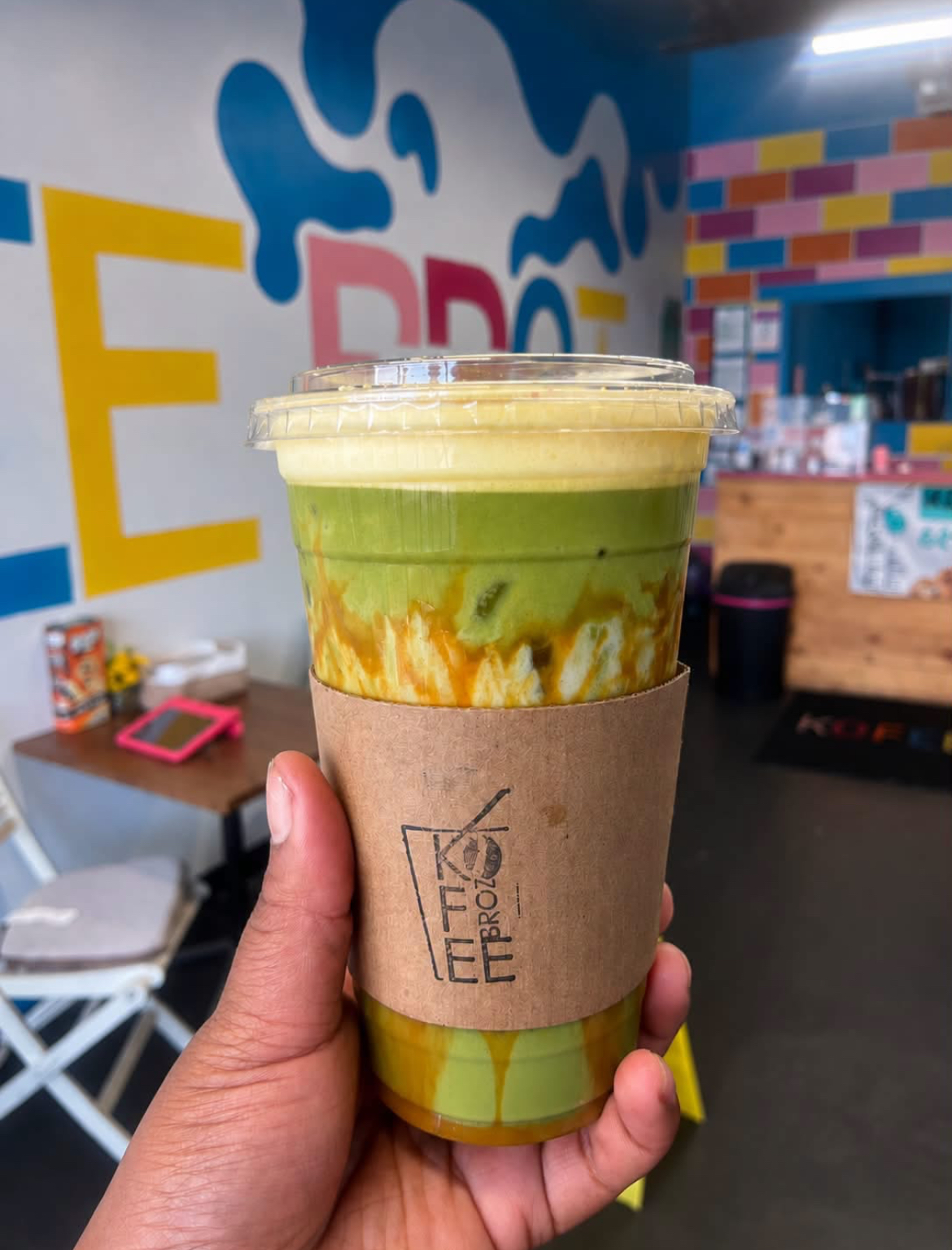 Iced matcha with caramel drizzle in a 24 oz Scholar Cup by the mural