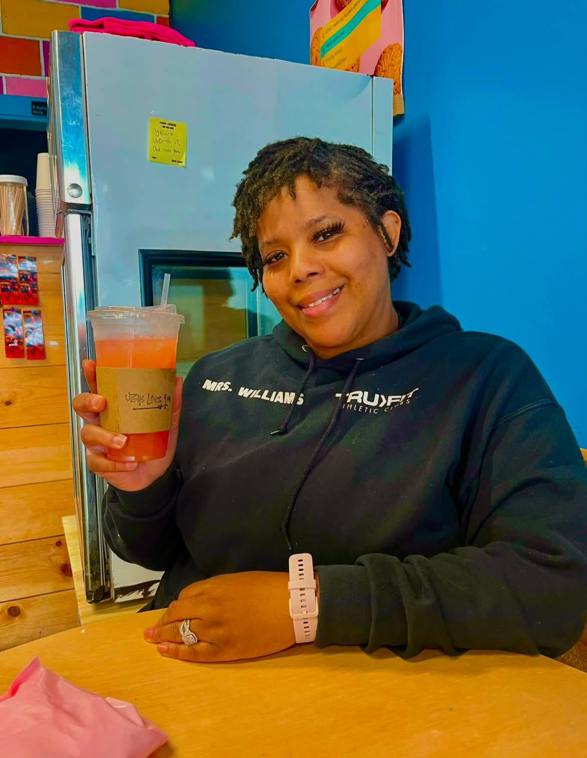 Guest smiling with a strawberry refresher in a Jesus Loves You sleeve