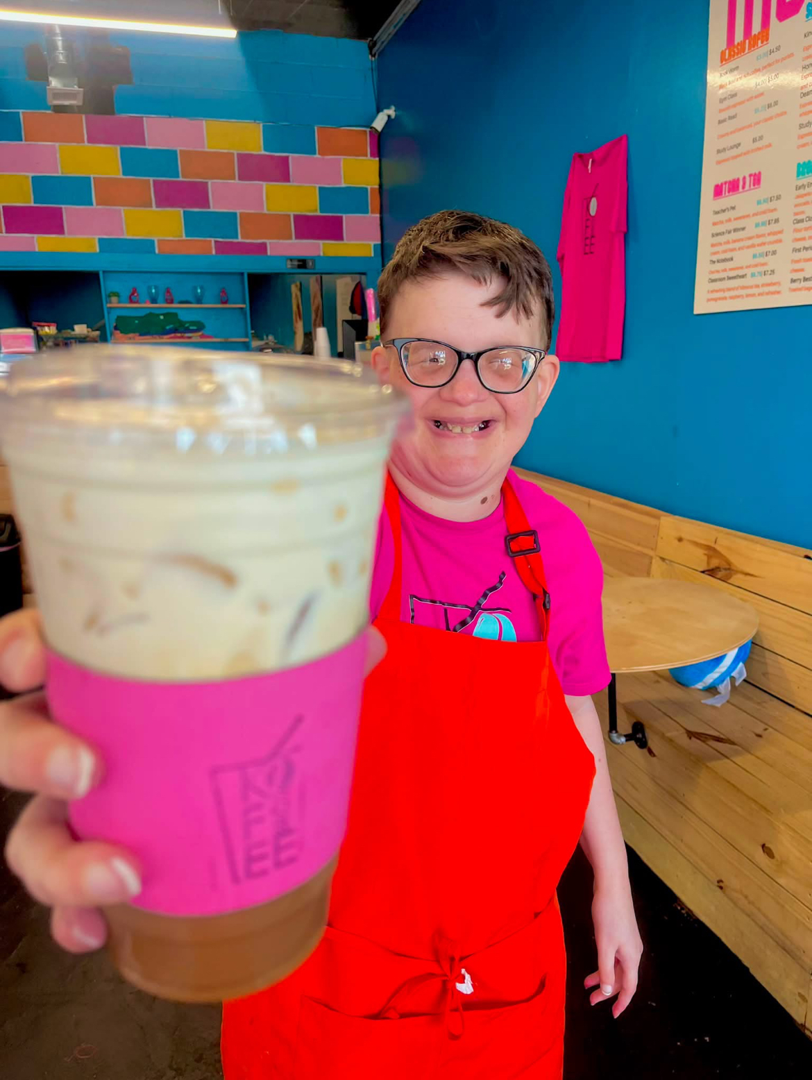 Shining Star barista in a red apron handing over an iced latte